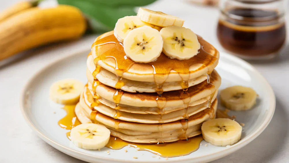 Plusieurs pancake empilé dans une assiette avec des banane dessus
