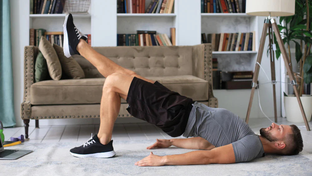 Homme athlétique en train de faire un exercice hip thrust une jambe dans sont salon en tenue de sport