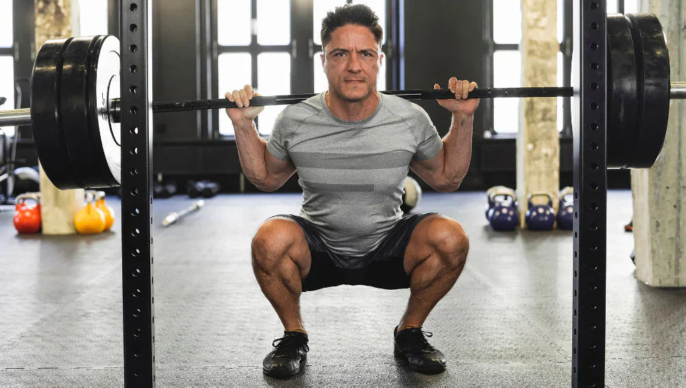 Homme musclé en train de faire du squat avec une barre olympique sur lui dans une salle de gym