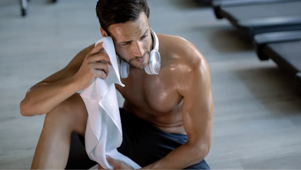 Homme torse nu assis par terre en train d'essuyer sa transpiration dans une salle de gym