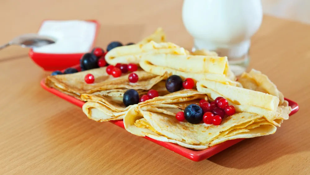 Crêpes posé sur une assiette rouge avec un bol a coté rempli de fromage blanc sur une table de bois