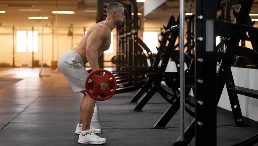 Homme musclé torse nu en train d'executer un mouvement de rowing barre dans une salle de gym