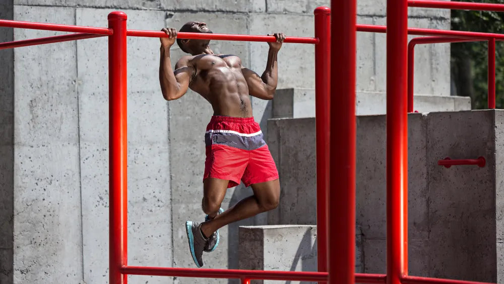 Homme musclé torse nu en train de faire des traction en pleine air