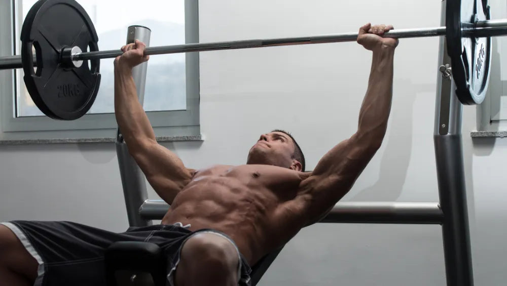 Un homme sec et musclé en train de faire un développer couché incliné à la barre olympique pour muscler le haut de ses pectoraux.