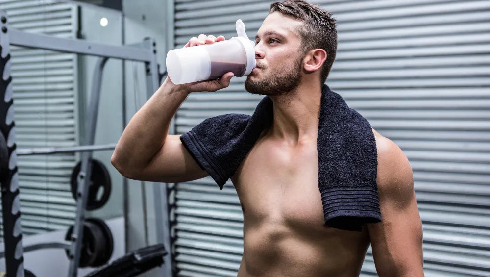 Homme torse nu dans une salle de sport buvant un shaker de whey