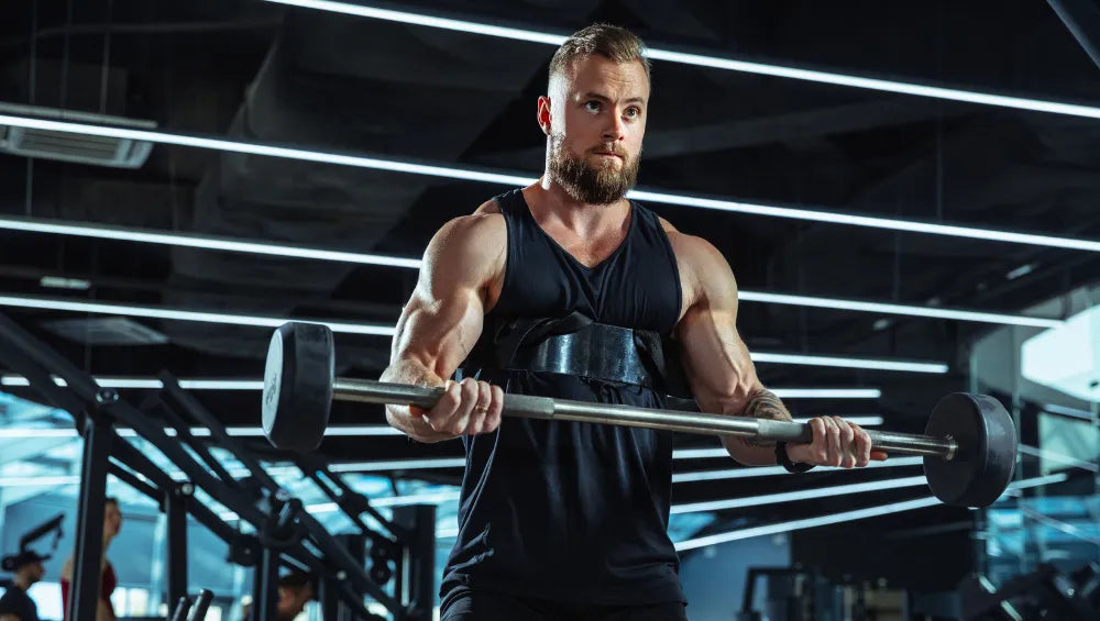 Homme musclé en train de faire du curl biceps à la barre dans une salle de gym