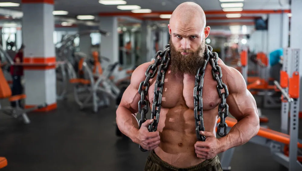 Homme torse nu sec et musclé en train de porter des chaines autours de son cou dans une salle de gym