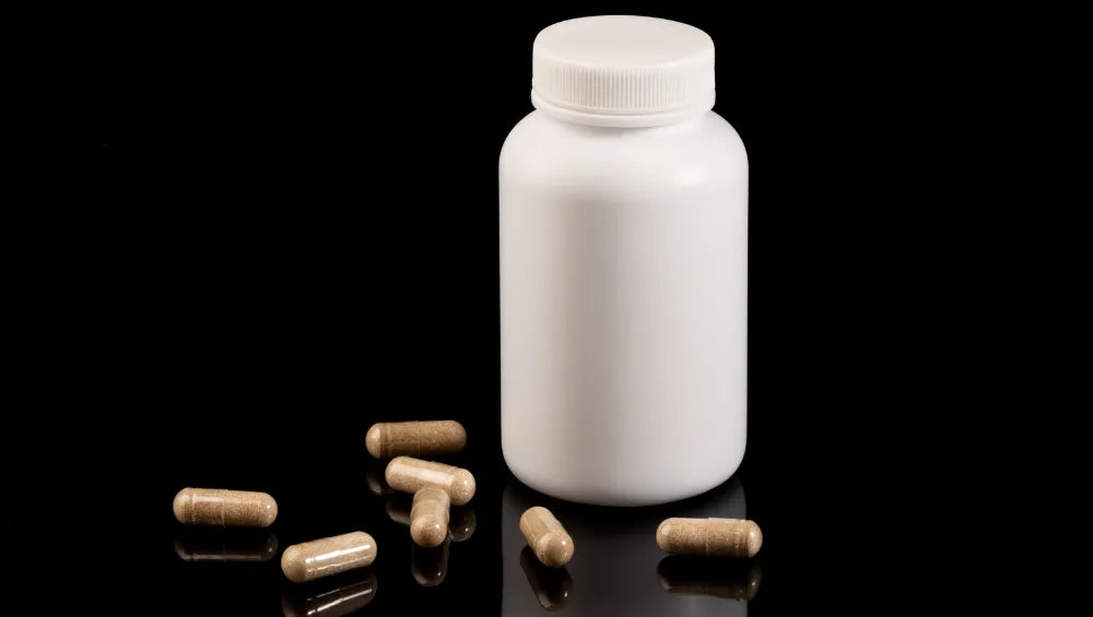 Un pilulier blanc sur un fond noir avec plusieurs pilules de couleur marron autour