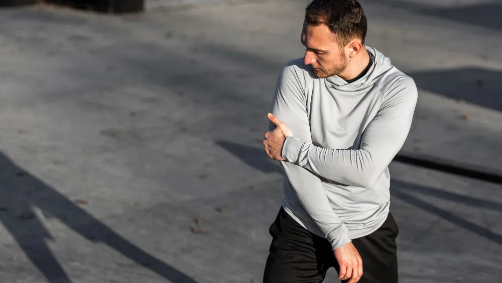 Un homme en pull gris en plein air ce tenant le triceps droit