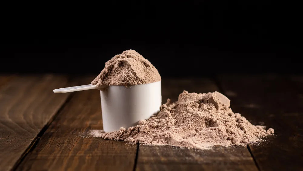 Une scoop de protéine avec de la poudre a coté sur un sol en bois