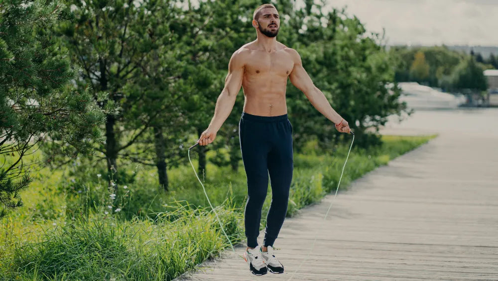 Homme musclé et sec torse nu en train de faire de la corde à sauté en pleine air