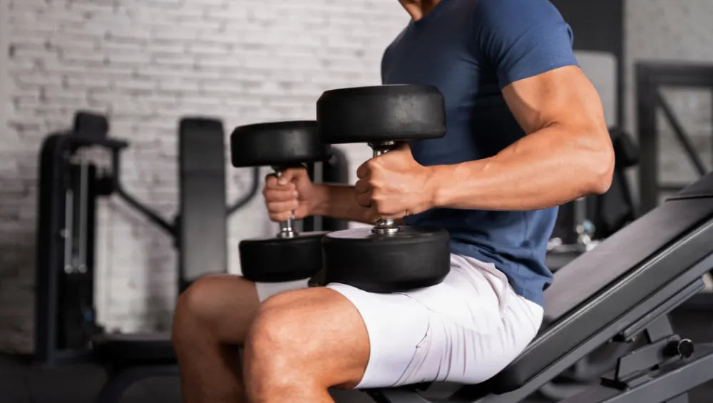 Homme musclé en short t-shirt assis sur un banc de developper couché incliné avec des haltères sur les genoux