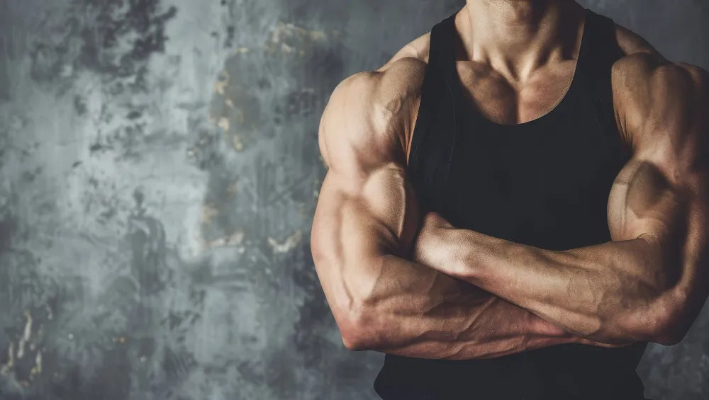 Homme musclé et sec en débardeur noir sur un fond gris avec les bras croisé
