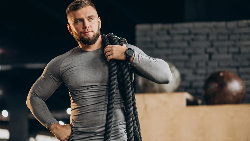 Homme qui est à la salle de sport, qui se prépare à faire son entrainement avec une corde épaisse.
