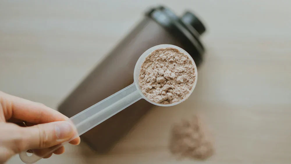 Une scoop de protein avec en fond un shaker posé sur une table