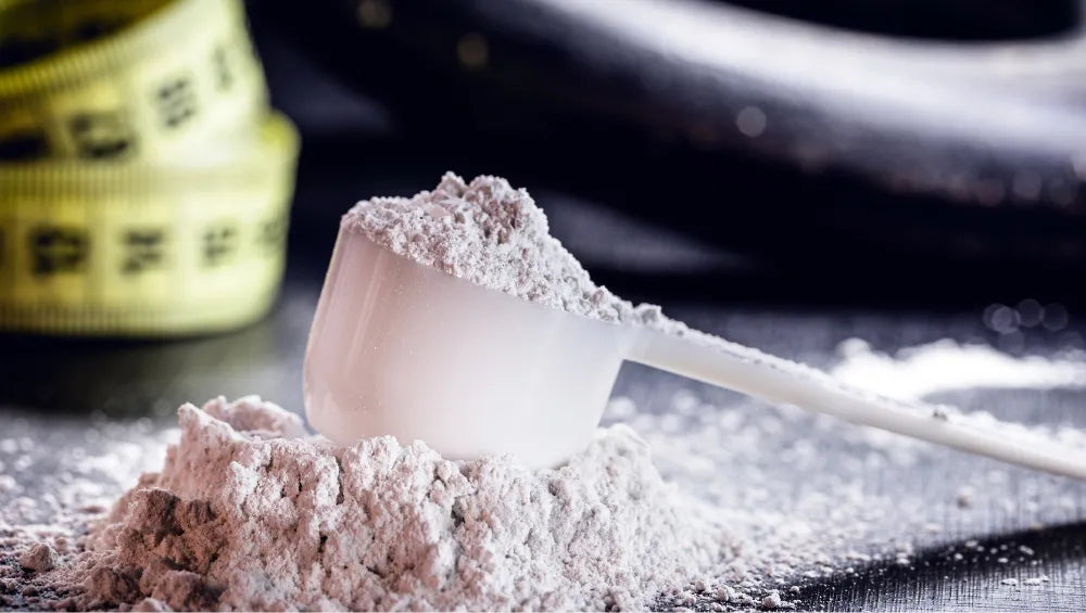 Une scoop de créatine avec en arrière plan un mètre souple ainsi qu'un poids de musculation