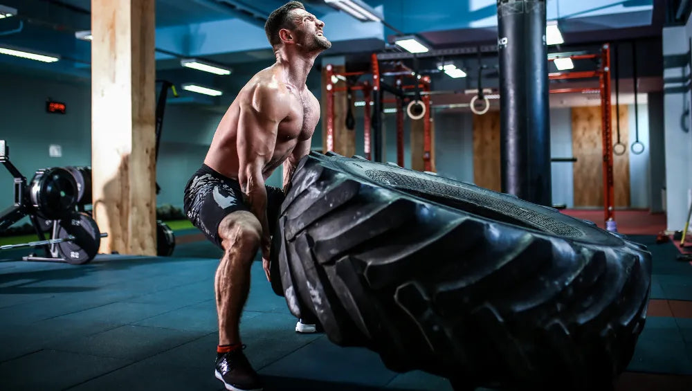 Homme musclé en short en train de soulevez un pneu poids lourd dans une salle de gym