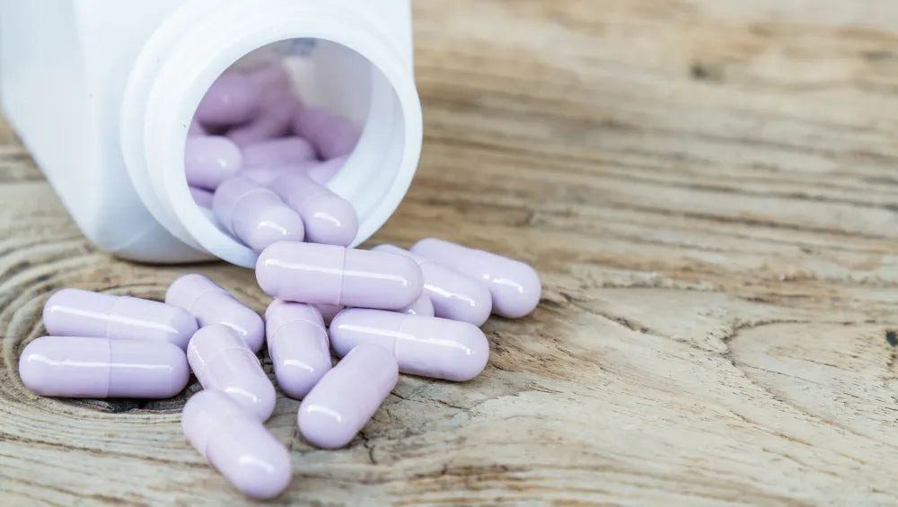 Pilulier blanc déversant des capsules violette sur une table en bois