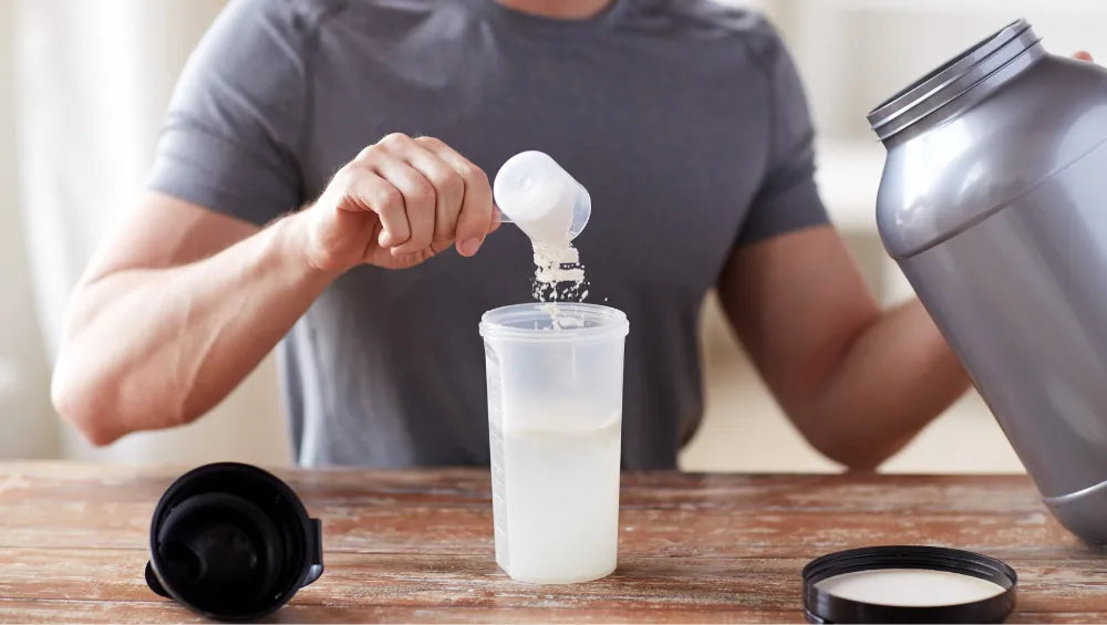 Homme en train de mettre une scoop de protein dans un shaker rempli d'eau sur un bar en bois