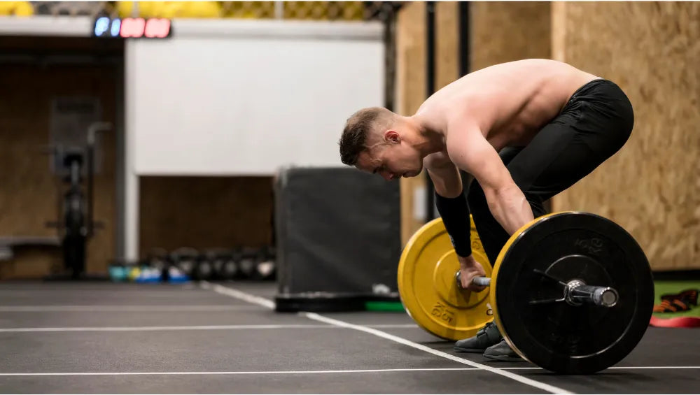Homme torse nu dans une salle de gym en train d'effectuer un mouvement de soulevez de terre