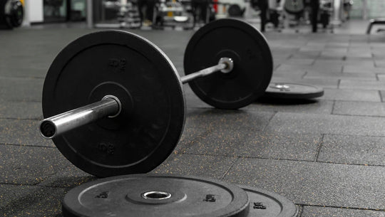 Image d'une barre de musculation au sol dans une salle de musculation.