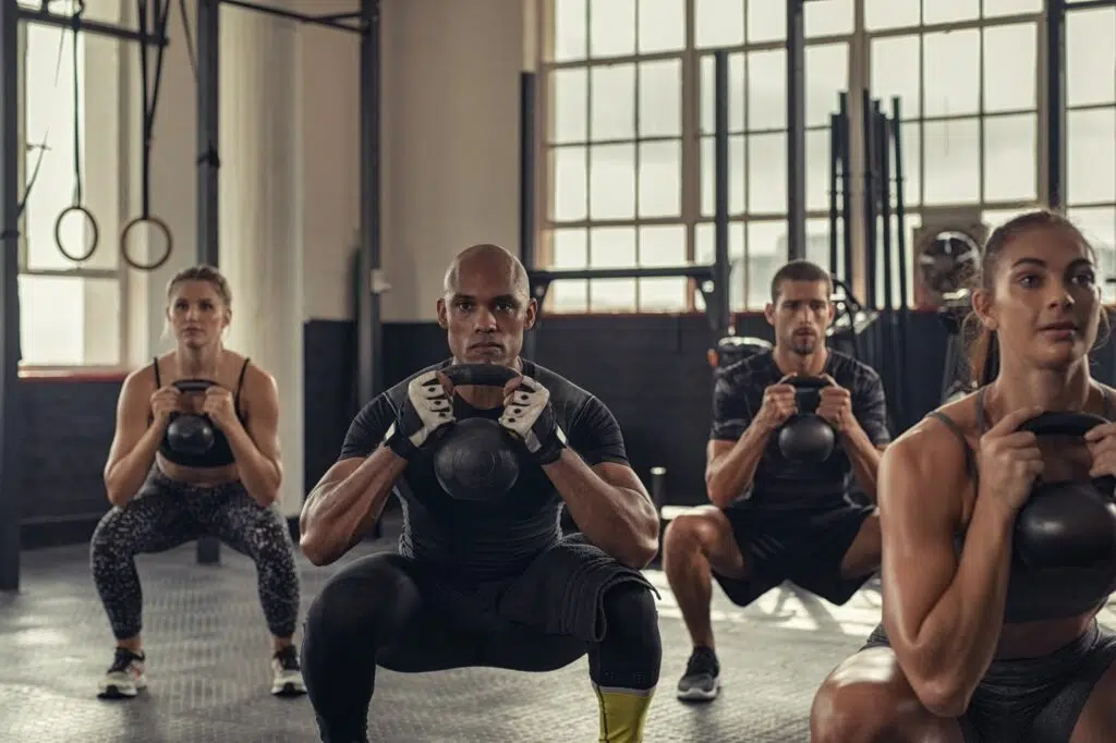 Des personnes en train de faire des squats et s'entrainant au CrossFit dans une salle de sport