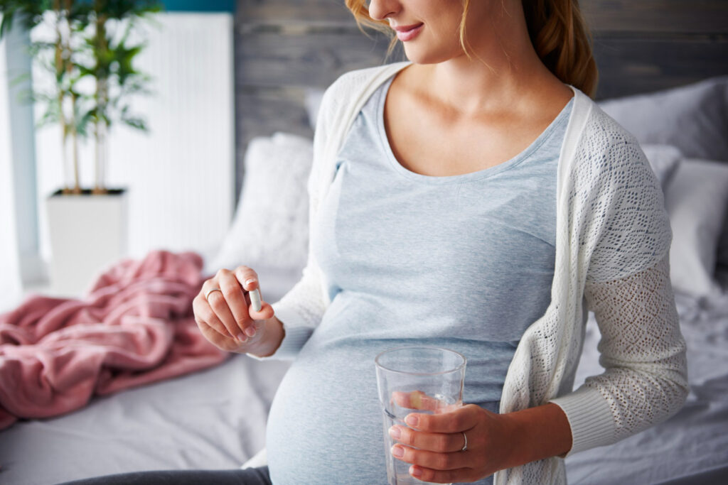 Une femme enceinte prenant une gélule de vitamine avec un verre d'eau.