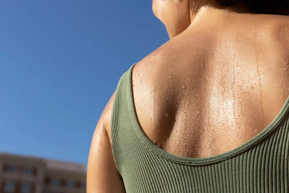 Back of a woman in a green tank top sweating under a blue sky