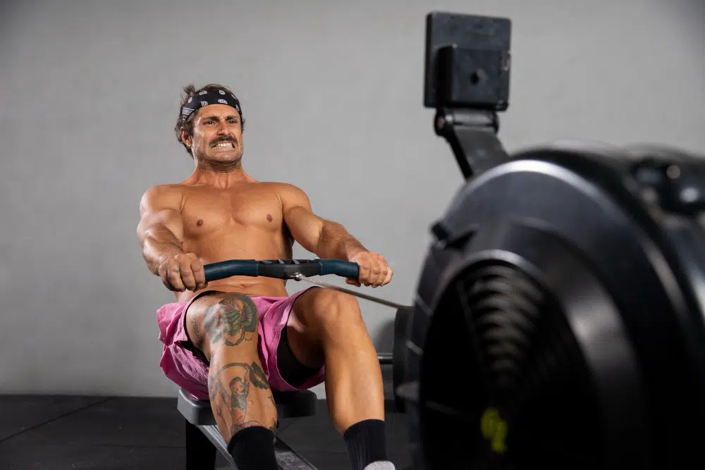 a shirtless man in pink shorts working on a rowing machine